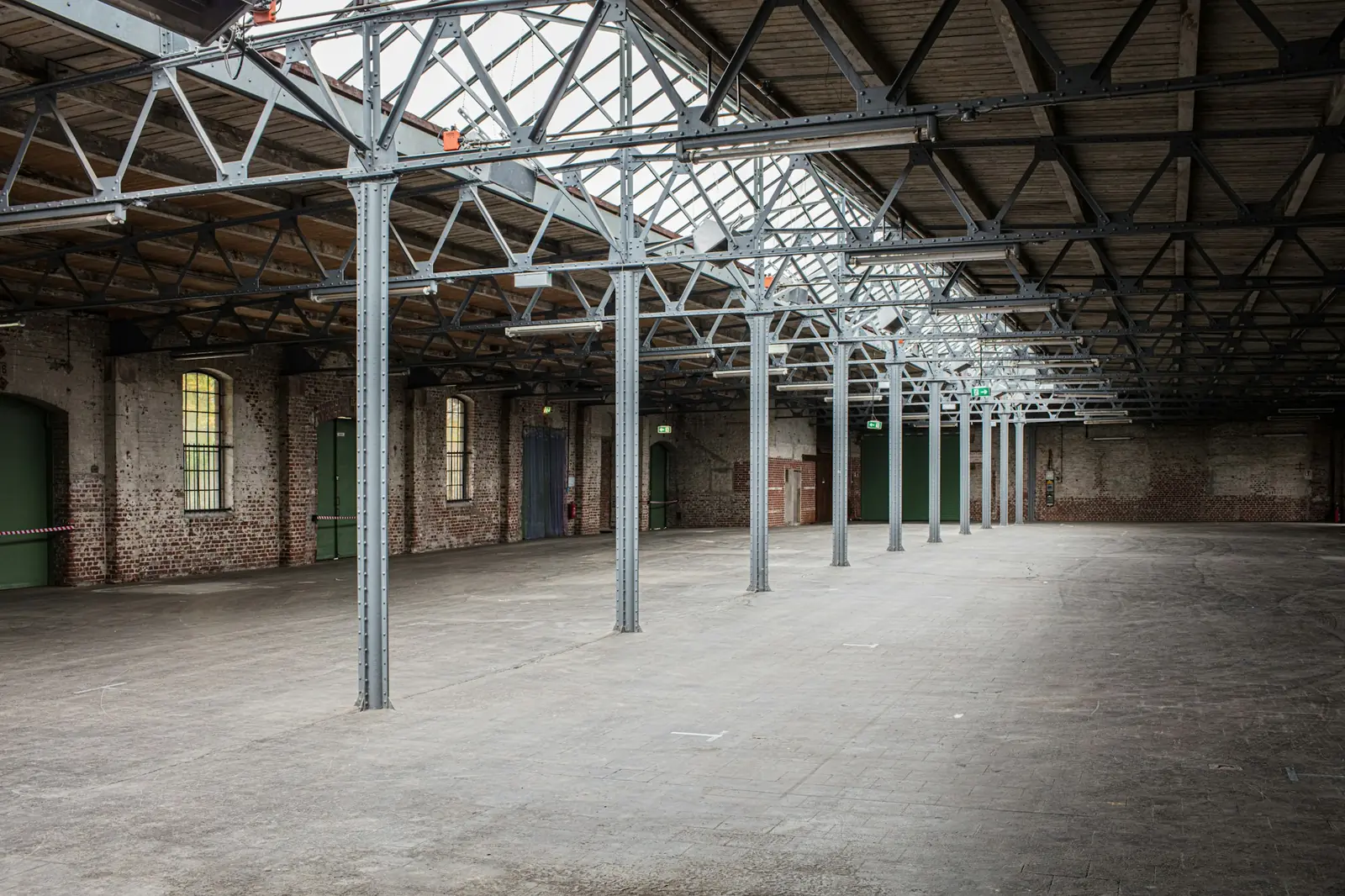 Leere Industriehalle mit Stahlstützen, Fachwerkbindern und Backsteinwänden, Symbolbild